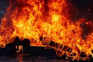 Obraz premium burnt car wheel, car accident, wheel in the fire, burnt tires, burning tires for protest. Fire close-up. Flame of fire. Hellfire.
