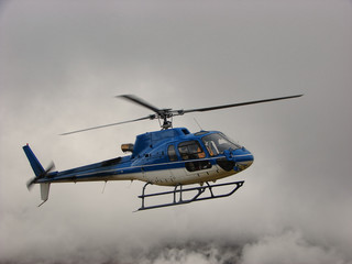 Blue helicopter flying in clouds