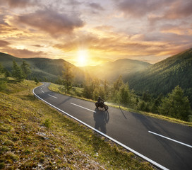 Motorbiker riding in Austrian Alps in beautiful sunset dramatic sky.