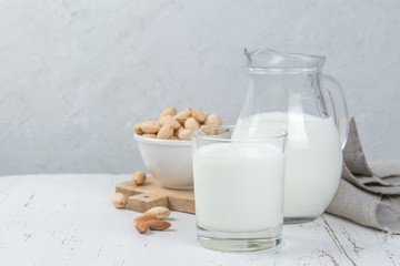 Almond milk in glass and jar on wood background
