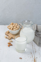 Almond milk in glass and jar on wood background