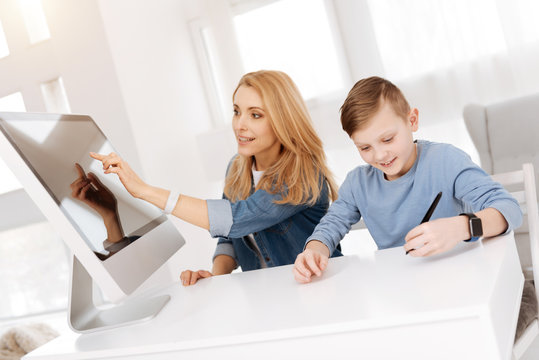 Digital device. Pleasant nice beautiful woman sitting together with her son and pressing the sensory screen while living in the smart house