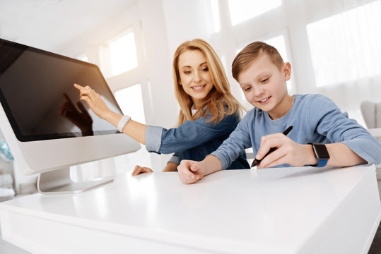 Young talent. Positive happy creative boy sitting at the table together with his mother and holding a stylus pen while drawing