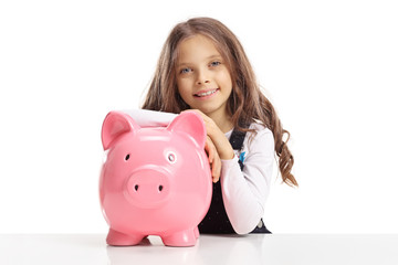 Little girl with a piggybank sitting at a table looking at the camera and smiling