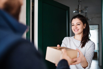 Woman receiving parcel from delivery man at the door. - obrazy, fototapety, plakaty