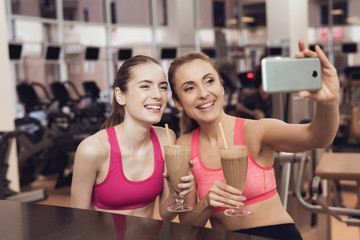 Mother and daughter drinking smoothies at the gym. They look happy, fashionable and fit.