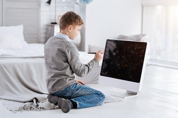 Digital device. Smart intelligent cute boy looking at the screen and holding a stylus pen and...