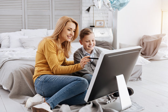 Progressive technology. Delighted positive young woman sitting together with her son and smiling while showing to him new technology