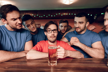 Blue team sports fans at bar surrounding red team fan at sports bar.