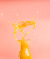 concept of healthy food, smoothies from oranges and bananas, splashes and drops fly out of the bottle, on a pink background, space for text