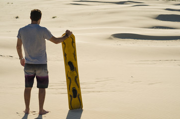 Young man on his back looking at the sand dunes, preparing to practice sandboarding.
