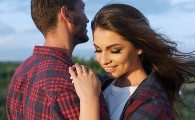 Horizontal cropped shot of happy couple have fun on a nature background. Rear view of handsome Caucasian guy wearing plaid shirt with smiling girlfriend hugs him. Lifestyle, people and travel concept.