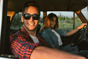 Portrait of happy romantic young couple going on a long drive in car on sunset light. Handsome young man wearing sunglasses with his beautiful girlfriend on a road trip. Travel, lifestyle concept.