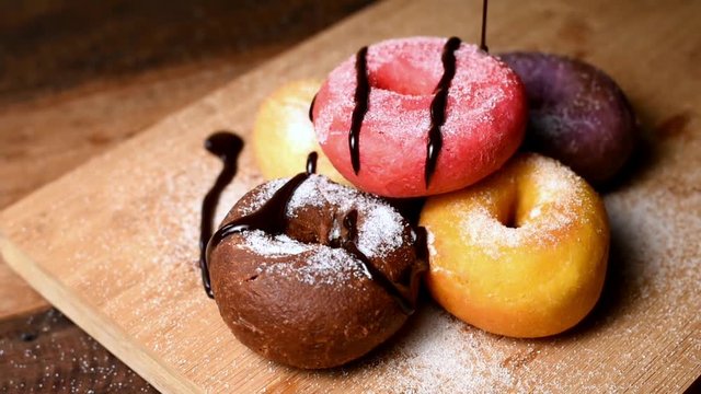 pouring melt chocolate on a assortment flavored of colorful homemade doughnut or donut on wooden table