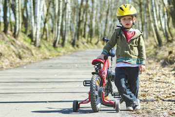 Little child boy cycling on bicycle in green park outdoor in spring. A child is riding a children's bike with support training wheels wearing safety helmet
