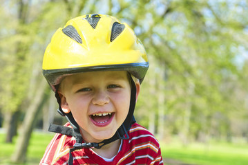 Little child boy cycling on bicycle in green park outdoor in spring. A child is riding a children's bike with support training wheels wearing safety helmet
