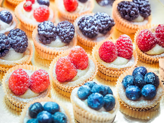 Many cakes with berries. Background of cupcakes with raspberries, blackberries and blueberries