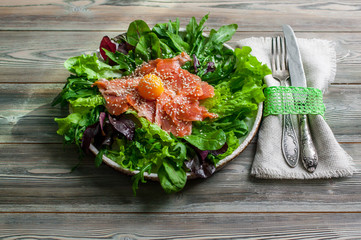 Salad of smoked salmon, egg yolk, fresh salad leaves, arugula, spinach and beet sprouts in a plate on a wooden background.