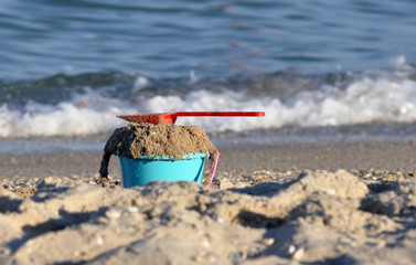 Children's toys are in the sand on the sea coast. A toy bucket, a rake and a shovel are buried in...