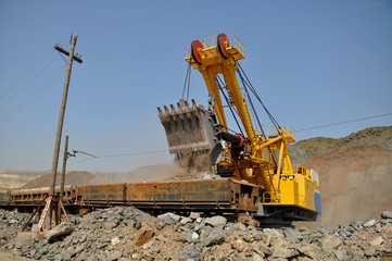 Obraz premium A large yellow excavator loads ore into a railway car