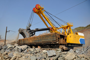 Fototapeta na wymiar A large yellow excavator loads ore into a railway car