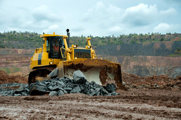 A yellow bulldozer builds a road in an iron ore quarry.