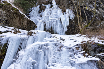 Fototapeta na wymiar Mountain slopes covered in ice and icicles as the winter snow is melting during cold temperature, forming ice waterfalls along the slopes