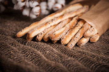 Delicious breadsticks grissini. Italian appetizers. Wooden dark background and burlap flowers of cotton