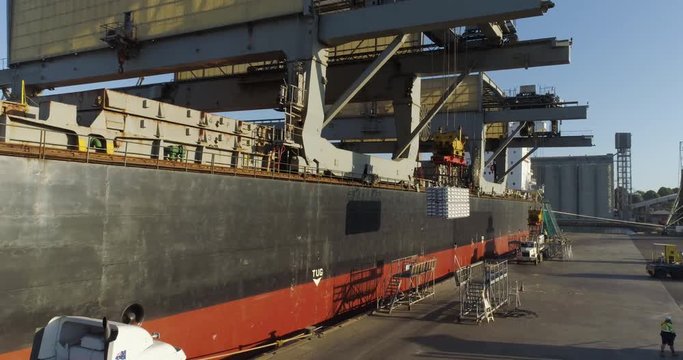 Drone tracking toward ship loading aluminium ingots at sunset for export from Australia - 4K 30P. 