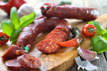 Spanische Spezialität: Luftgetrocknete scharfe Chorizo Paprikasalami auf Olivenholzbrett serviert – Spanish salami: Spicy chorizo sausage with tomatoes and basil served on an olive wood cutting board