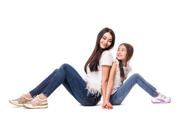 Beautiful and happy young mother with her small daughter sitting on the floor back to back and look each other isolated on white background.