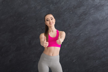 Fototapeta na wymiar Happy sporty woman showing thumb up on grey background