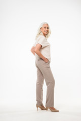 Full length portrait of beautiful adult woman 70s with gray hair smiling and looking on camera with arms in pockets, isolated over white background