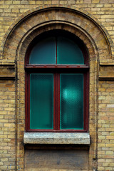 Vintage arched window in the wall of yellow brick. Green - the colors of sea wave glass in a maroon dark red wooden frame. The concept of antique vintage architecture in building elements.