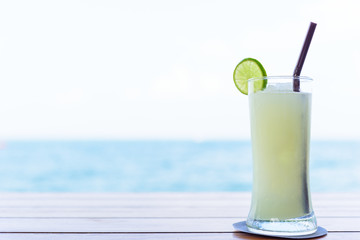 A glass of lemon juice on the brown wood table with seascape and sky background in the morning with vacation and relaxing time.