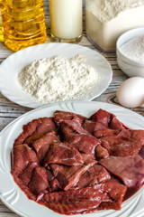 Raw liver on a white plate on a wooden background. A set of products for cooking fried liver egg oil salt flour. Food ingredient. Selective focus.