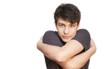 A cute teen on a white background embraces himself. Isolated