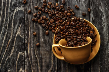 A coffee cup with coffee beans on an old wooden table. Fried coffee beans on a wooden background. Viewing from above.
