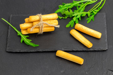 Crispy bread sticks with arugula, bread sticks on black stone background with copy space