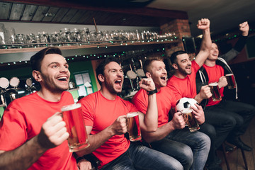 Soccer fans sitting in line celebrating and cheering drinking beer at sports bar.