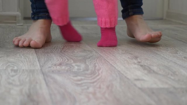 legs of child and mother go on floor, little baby takes first steps