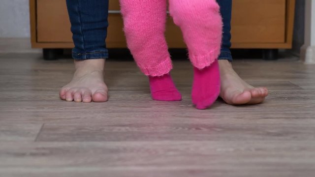 little baby takes first steps, legs of child and mother go on floor