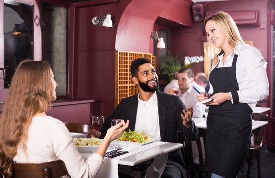 waitress serving meal for young couple at table