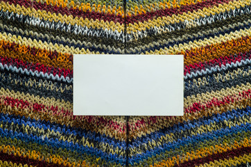 Colorful Knit Fabric Texture with White Card of Paper as Blank Space. Macro View of a Knitted Sweater. Blank Backdrop Mock-Up
