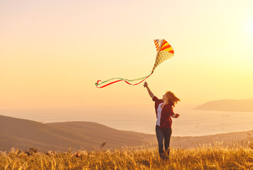 Happy young woman running with kite on glade at sunset in summer.