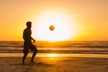 Great concept of soccer, man playing soccer on the beach in golden hour, sunset. Making keepie uppie.