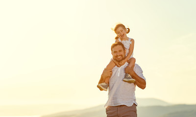 father's day. child daughter sits on her dad shoulders outdoors on a summer .