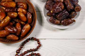Dates fruit and rosary on white wooden table. Top view
