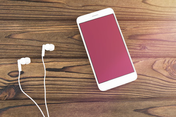 smartphone with a pink screen, headphones on a wooden background. music melodies internet