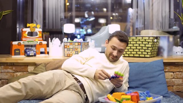 Funny adult man plays with kid constructor in children's room in cafe